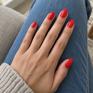 Hand mit roten Mandelnägeln in Ferrari Rot auf einer blauen Jeans.