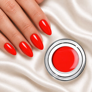 Nageldesign in Kuss Rot neben einem offenen Farbgel-Tiegel auf weißem Stoff