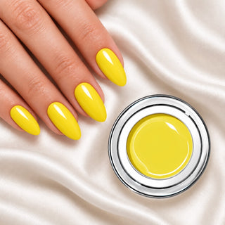 Nageldesign in Nude Gelb neben einem offenen Farbgel-Tiegel auf weißem Stoff