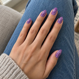 Nageldesign in Disco Lila – Hand mit lackierten Nägeln auf blauem Jeansstoff