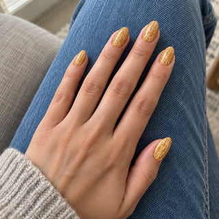 Nageldesign in Disco Gold – Hand mit lackierten Nägeln auf blauem Jeansstoff