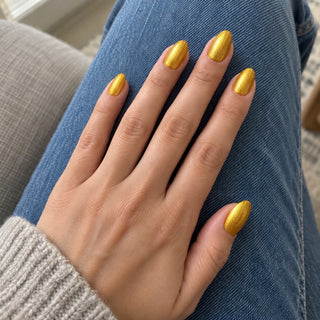 Nageldesign in Metallic Gold – Hand mit lackierten Nägeln auf blauem Jeansstoff