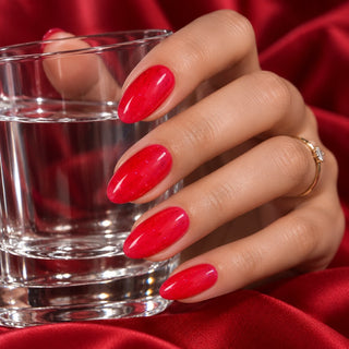 Hand mit rosenroten Glitzernägeln hält ein Wasserglas vor rotem Satin – Gellack 90002 von Rockstar Nails.