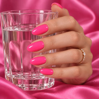 Hand mit glänzenden Nägeln in Neon Pink hält ein Wasserglas vor pinkem Satin – Rockstar Nails Gellack 90020.