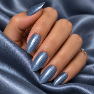 Hand mit glänzenden Nägeln in Glimmer Blau Grau auf blauem Satin – Rockstar Nails Gellack 90233.